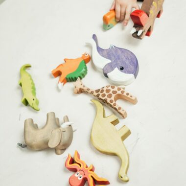 A child plays with a variety of colorful wooden animal toys on a white table indoors.