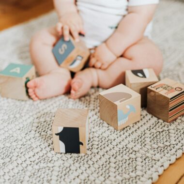 Adorable baby sitting on a rug and playing with colorful wooden blocks.