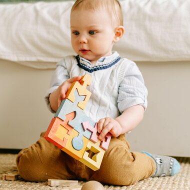 Cute baby in a home setting plays with a colorful wooden puzzle on the floor.